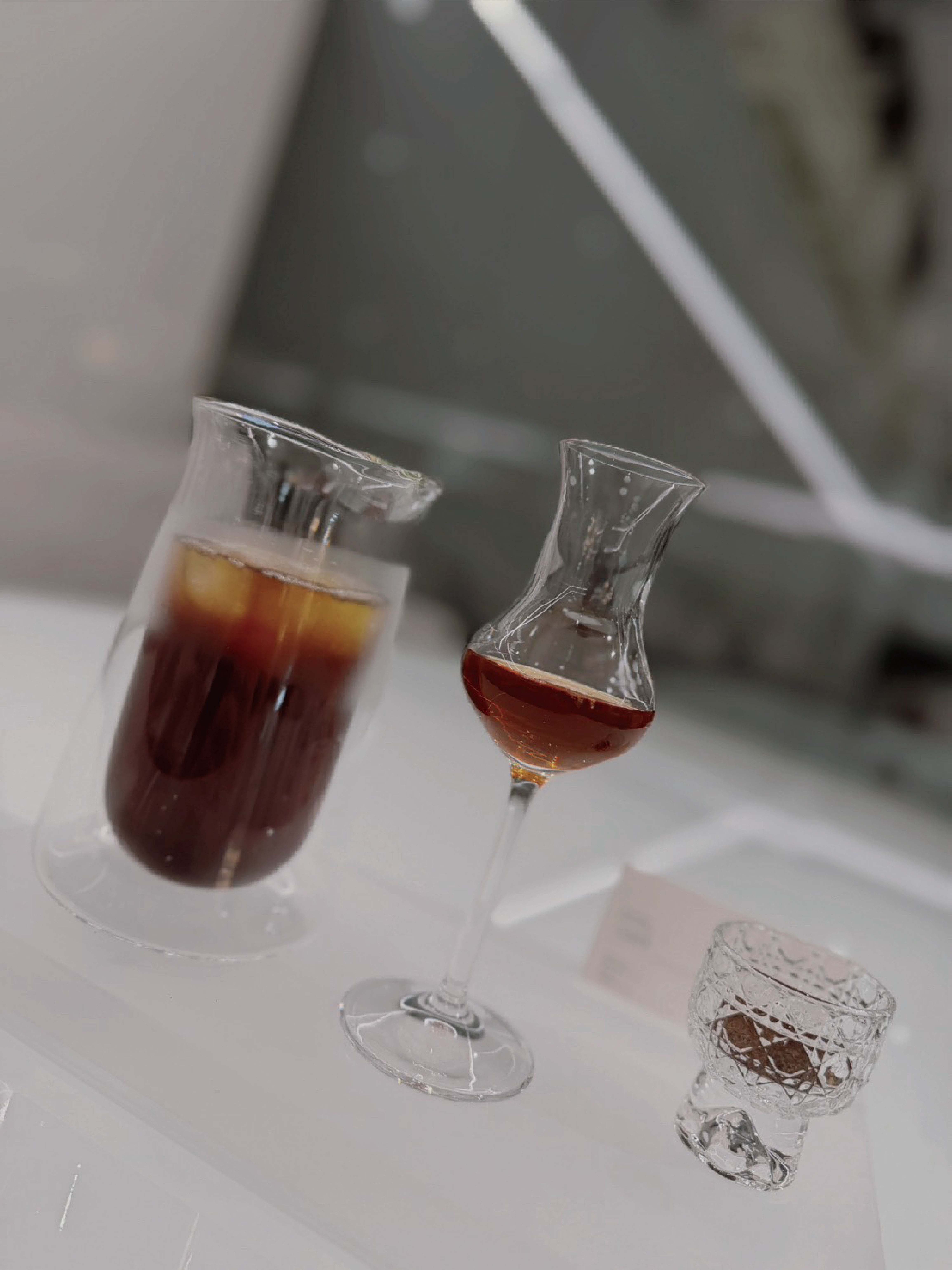 不同於 KA SKY COFFEE 的全開放式白色空間，KA COFFEE LOUNGE 微風信義店以黑、灰、白三色交織，打造全新的咖啡酒廊型態。銀灰色金屬垂簾劃分出若隱若現的半通透空間，搭配環繞全區的氣氛光感設計，以直覺為起點、平衡為核心，讓俐落線條與大面積留白彼此映照，在開放與私密、光與影之間取得平衡，透過線條、材質與光感的自然交織，形塑極簡而充滿感知的空間。  以居中的全白色吧台為視覺起點向外延伸，色彩由白轉灰，再逐步過渡至鐵灰色亮牆，透過色彩與材質的層層遞進，如同由明入暗、由日間走向夜晚的空間流動。咖啡與酒飲隨著光影更迭，在日與夜之間自然轉換，讓每一次停留都成為一場關於風味、感知與生活的漫遊，留下屬於 KA COFFEE LOUNGE 的感官記憶。